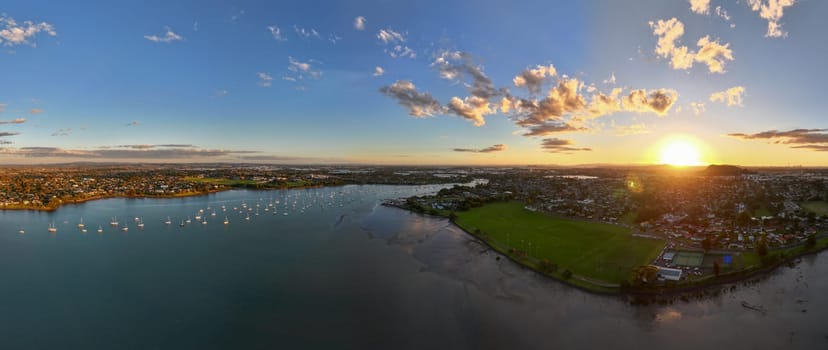 Drone shot of the Tamaki river with cloud reflections at sunset. Sailboats on moorings line up the river and marina in New Zealand