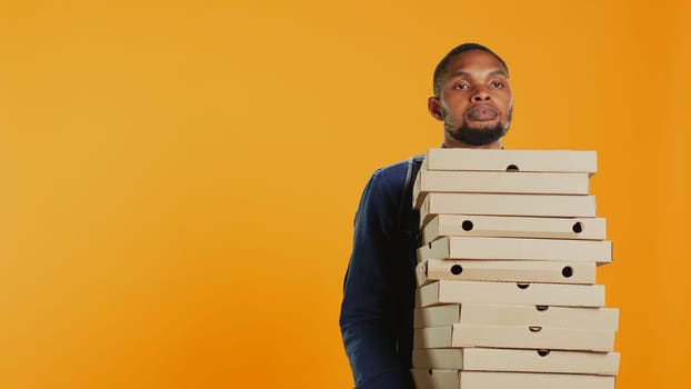 Clumsy deliveryman dropping a huge stack of pizza boxes in studio, wasting a lot of food and making a mess. Young distressed man makes a mistake and spills a large pile of fast food. Camera B.