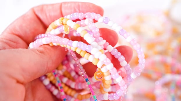 Delicate fingers of a young girl navigate through a treasure trove of bright, multicolored beads, each compartment revealing a new hue to choose from. She's immersed in the joyful task of stringing together a handmade bracelet, with golden beads and pearls lying nearby to add a touch of sparkle to her creation.