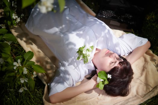 Girl Relaxing, sleeping near Blossoming apple Tree on Sunny Day. Portrait of Middle aged woman enjoying nature surrounded near white blossoms