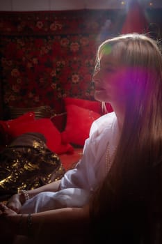 Beautiful European girl looking like Arab woman in red room with rich fabrics and carpets in sultan harem. Photo shoot of an oriental style odalisque. A model poses in sari as indian woman in india