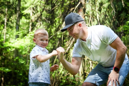 Father and Son Enjoying Playful Fist Bump in Lush Forest. A joyful moment as a dad and his young son exchange a fist bump in the woods