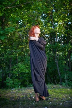 Elegant senior mature Woman dancing in Black Dress in green park. Woman with red hair posing on nature