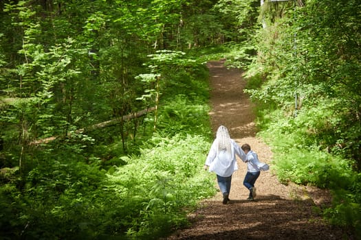 Funny mother with dreadlocks and fat boy happy walking in the forest on a sunny summer day