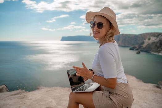 Freelance women sea working on the computer. Good looking middle aged woman typing on a laptop keyboard outdoors with a beautiful sea view. The concept of remote work