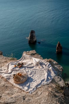 A white blanket is spread out on a beach near the water. The blanket is on a rock and there are some oranges and apples on it. The scene is peaceful and relaxing, with the ocean in the background