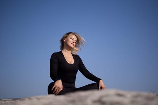 A woman is sitting on a rock and looking up at the sky. She is wearing a black shirt and black pants. The sky is blue and clear