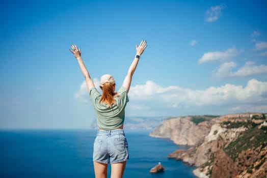 Woman tourist sky sea. Happy traveller woman in hat enjoys vacation raised her hands up.