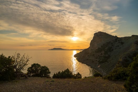 A beautiful sunset over the ocean with a mountain in the background. The sky is filled with clouds and the sun is setting