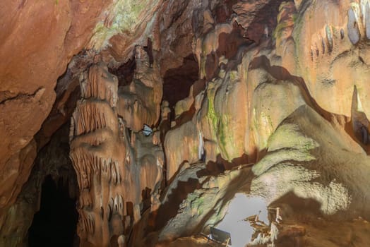 A cave with many stalactites and stalagmites. The cave is dark and the light is coming from the outside