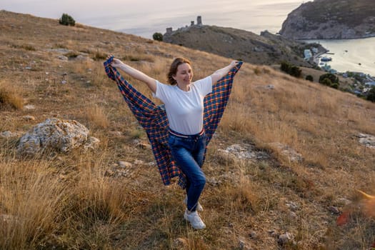 A woman is standing in a field with a blanket draped over her shoulders. She is smiling and she is enjoying the outdoors