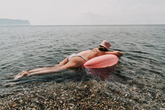 A woman is laying on a pink inflatable tube in the ocean. The water is calm and the sky is cloudy