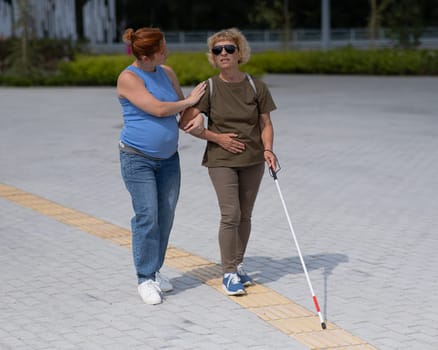 Caucasian pregnant woman leading blind elderly lady outdoors