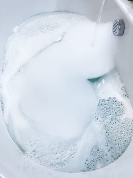 Elegant white bathtub filled with water, featuring a sleek brushed nickel faucet with water flowing gently into the tub. The bathtub’s modern design and the clear, tranquil water suggest a peaceful bathroom setting.