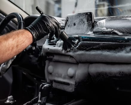 A mechanic cleans the interior of a car with a brush and foam