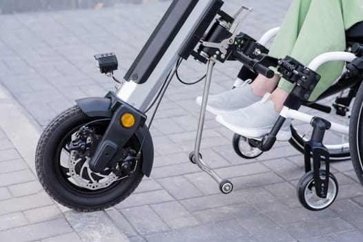 A faceless woman in a wheelchair with an assistive device for manual control. Electric handbike