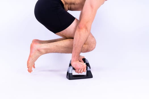 Shirtless muscular athlete do push-up on push up bars. Full body man on white studio background.