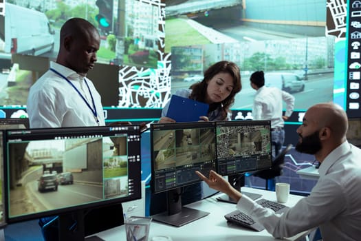 Diverse team of supervisors overseeing their staff activity on gps locating, following delivery truck drivers around in traffic via satellite map. Operators guiding couriers on routes.