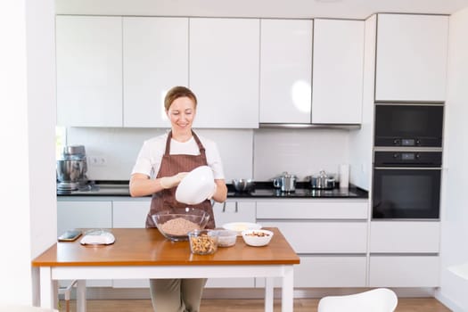 A woman is standing in a kitchen, preparing food. She is wearing an apron and has a smile on her face. The kitchen is clean and well-organized, with various appliances and utensils