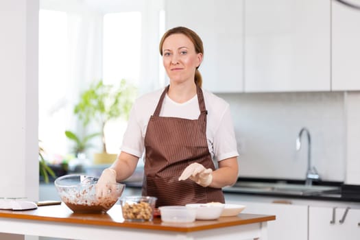 A woman is standing in a kitchen, wearing an apron and preparing food. She is smiling and she is enjoying herself. The kitchen is well-equipped with various utensils and appliances, including a sink