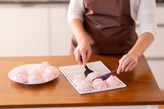 A woman is cutting a tray of pink pastries on a wooden table. The pastries are arranged in a grid pattern on the tray