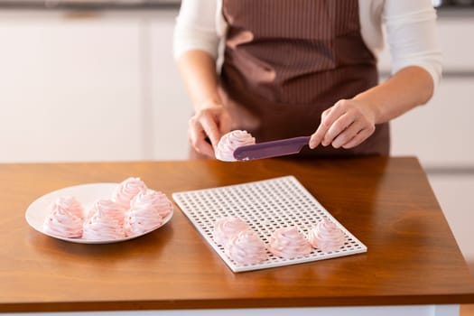 A woman is cutting a dessert on a wooden table. She is using a spatula to cut the dessert into small pieces. The dessert is pink and looks delicious