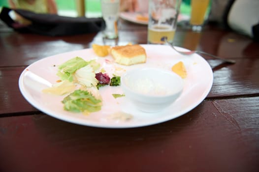 Leftover food on a white plate on wooden table, close-up. Food and drink consumerism. View from above