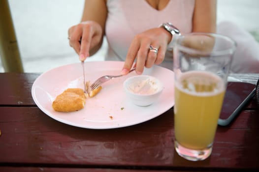Woman's hands using fork and kitchen knife, cut fried cheese. A cup of beer on table on foreground. The concept of eating out. Restaurant food nd drink. Slovak food