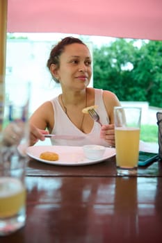 Smiling happy female tourist eating out, tasting delicious Slovak food in an outdoors restaurant. Multi ethnic young woman holding a fork