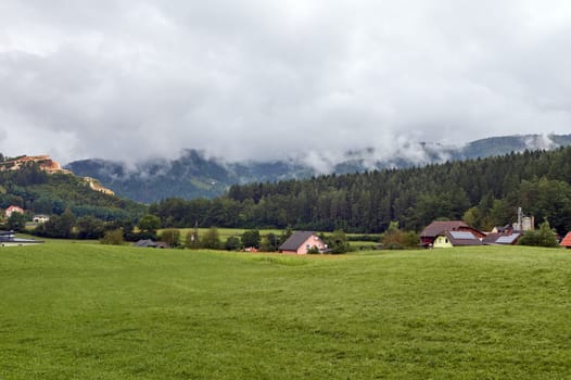 Beautiful mesmerizing view of a village with houses and chalets in pastures in Slovak Carpathians ridge on a foggy day. Nature background. Landscape scenery. Tourism and travel destinations concept.