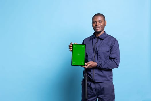 Security officer holding a device with greenscreen display in studio, posing with safeguarding uniform on camera. Guard presenting a tablet with greenscreen layout, uniform equipped with baton.