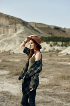 serene woman in plaid shirt and hat standing amidst desert landscape with majestic mountains in background