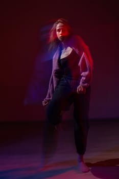 A young woman dances contemporary dances in blue and red light. Long exposure. Vertical photo
