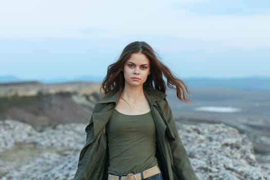 serene woman in green jacket stands atop mountain overlooking ocean horizon