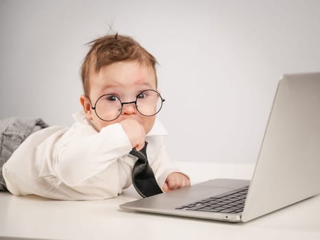 Cute baby in glasses and suit working on laptop