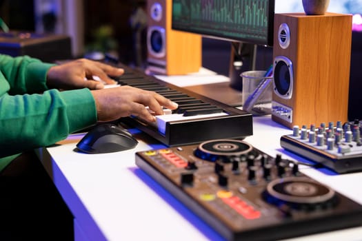 Music producer plays electronic keyboard piano notes over a recording in home studio, producing new tracks for an album. Artist technician mixing and mastering his own songs. Close up.