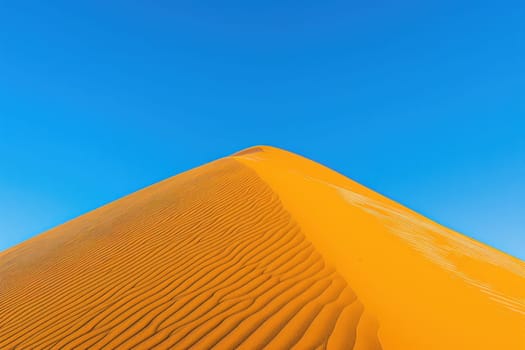 Spectacular desert sand dune landscape with vibrant orange colors and clear blue sky in sahara travel adventure concept