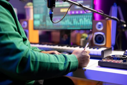 Musician taking notes on paper to produce a new track, making rhymes and blending musical elements together. Producer songwriter composing new melodic verses for a tune. Close up.