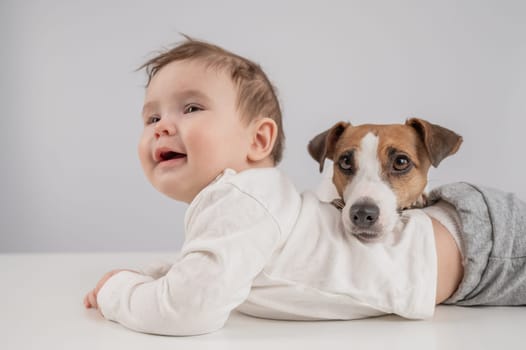 Cute baby boy and Jack Russell terrier dog lying in an embrace on a white background