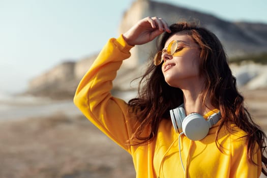 Serene sunset beach vibes young woman in yellow sweater and sunglasses enjoys music by the ocean