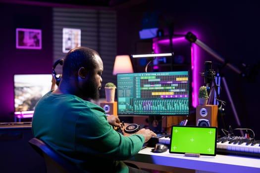 Professional sound engineer editing his music to enhance sound quality, using a greenscreen on tablet. Producer mixing and mastering tunes in his home studio, acoustical engineering.