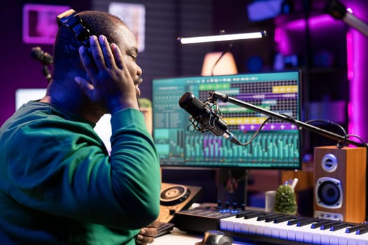 Creative artist songwriter recording his voice and lyrics in home studio, working on creating new soundtracks with microphone and stereo gear. Musician performing a tune, edit with mixing console.