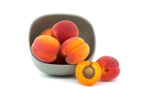 Bowl filled with ripe whole apricots and one cut in half to reveal its interior, isolated on a white background