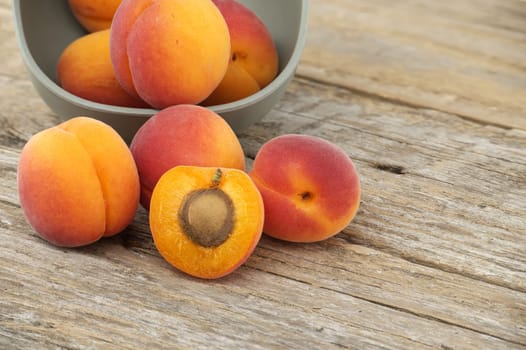 Group of fresh whole apricots and one cut in half to reveal its interior, rustic wooden table