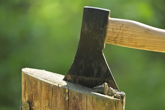 Hatchet embedded in a log of wood against blurred background with dominant green hues