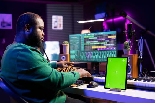 Audio technician composing new tracks with digital mix master software, having a tablet with isolated copyspace on desk. Professional engineer editing music in post production.