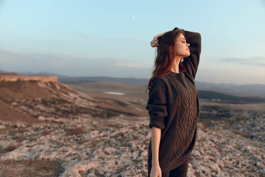 Woman in awe on mountain peak gazes at the sky with hands on head