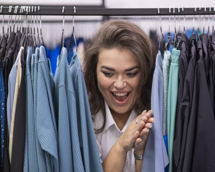 A fat woman in a plus size store peeks out from behind racks of clothes