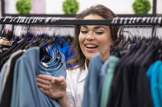 Portrait of a fat woman in a plus size store through hangers with clothes