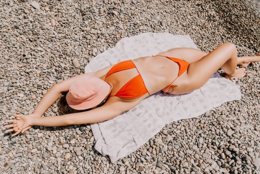 Happy smiling young woman with straw hat sunbathing or tanning on a seaside beach during summer vacation. Slow motion of happy tourist in red swimsuit on black lava sand beach green palms background